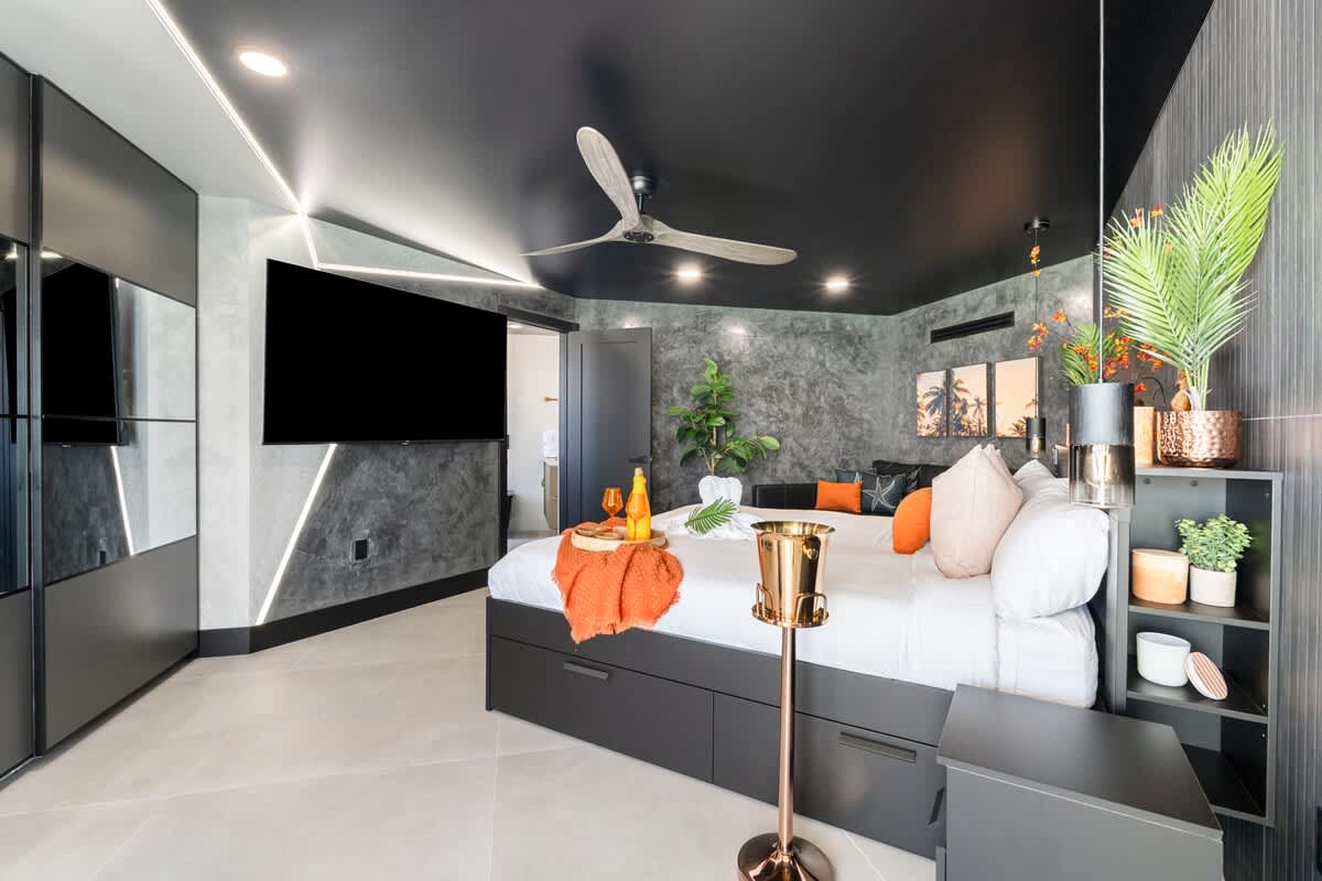 The Summit Penthouse 1501 – Modern penthouse bedroom featuring a king bed, wall-mounted TV, and decorative plants against a textured wall.