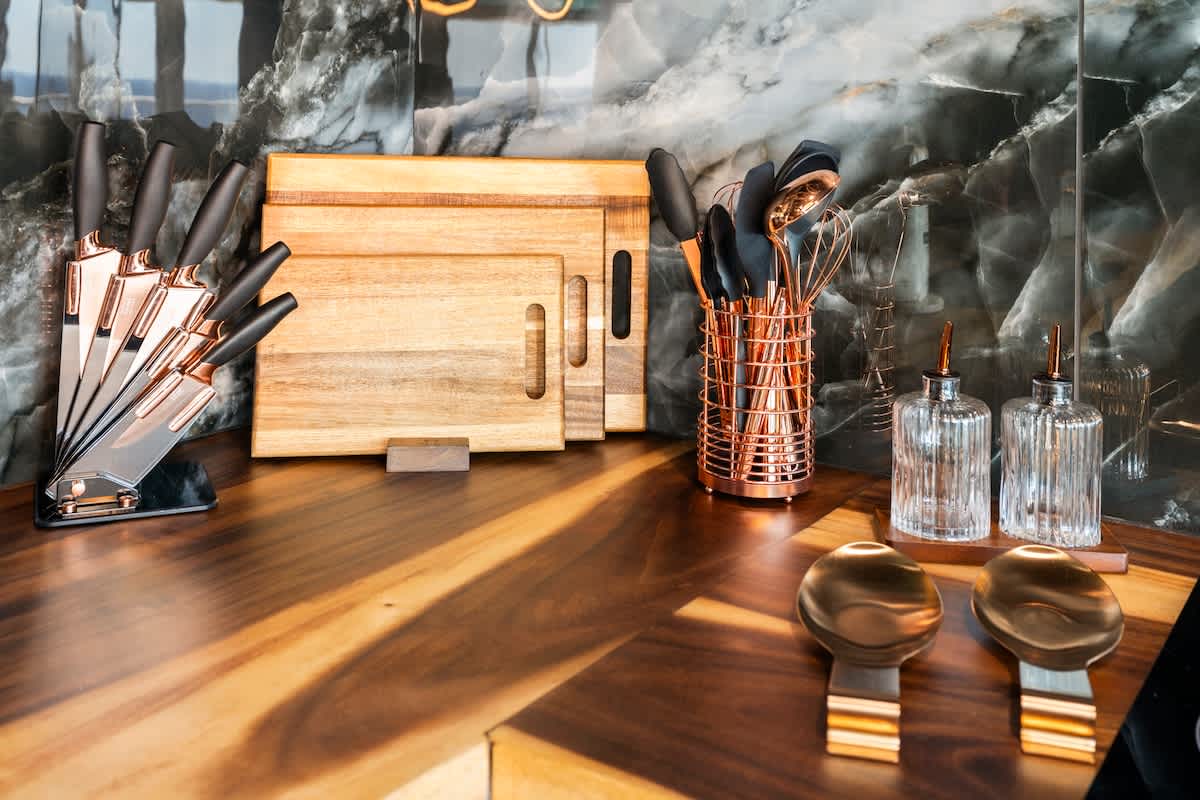 The Summit Penthouse 1501 – Modern kitchen countertop with wooden cutting boards, knife set, utensils, and glass containers against a dark marble backdrop.