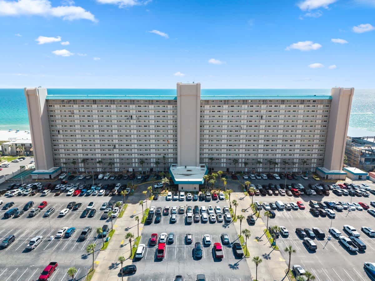 The Summit Penthouse 1501 – Exterior view of a beachfront hotel, with parking lot visible and ocean in the background.