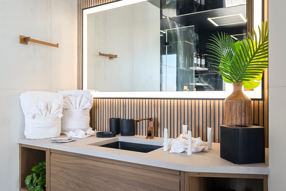 The Summit Penthouse 1501 – Modern bathroom with a dark sink, decorative towels, and a large illuminated mirror.