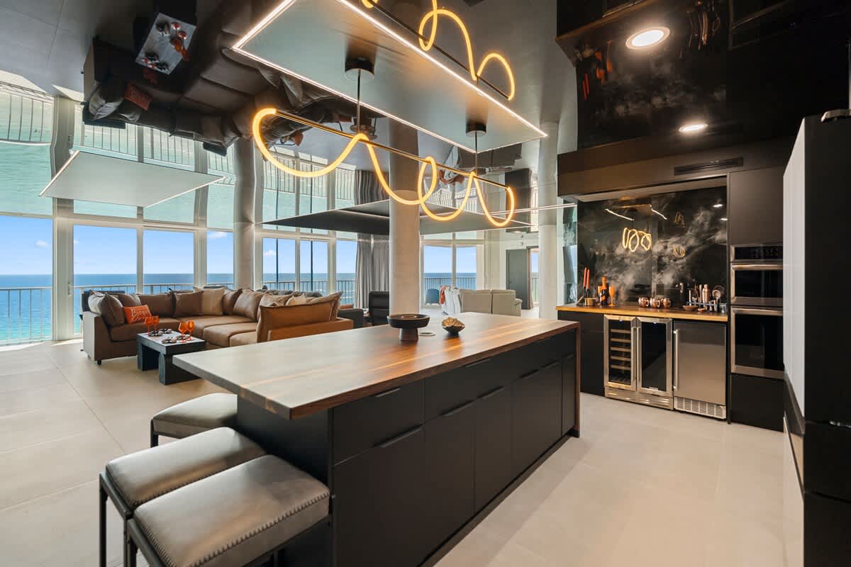 The Summit Penthouse 1501 – Open-concept living area with a large sofa, modern kitchen, and ocean views through floor-to-ceiling windows.