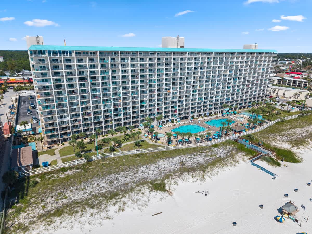 The Summit Penthouse 1501 – Aerial view of a beachfront resort with pools, palm trees, and a white sandy beach.