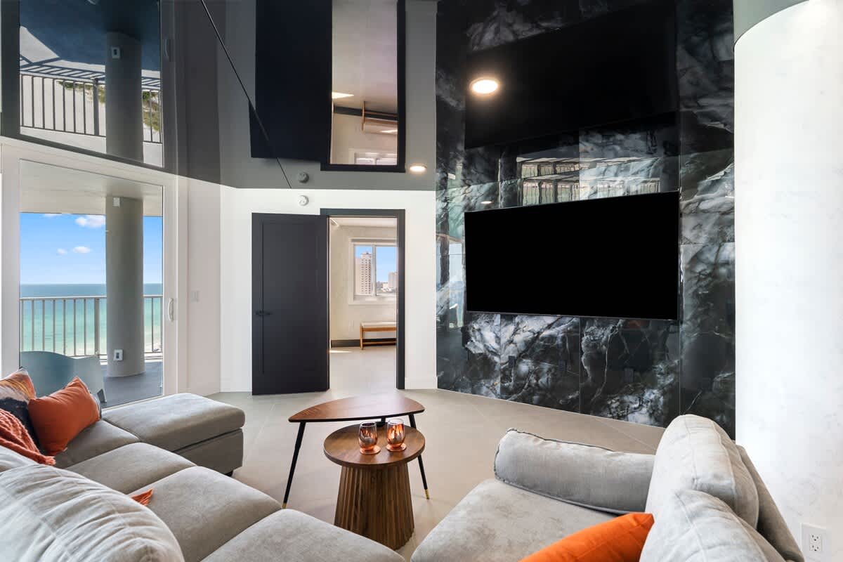 The Summit Penthouse 1501 – Living room with large windows, ocean view, gray couch, coffee table, and a marble feature wall.