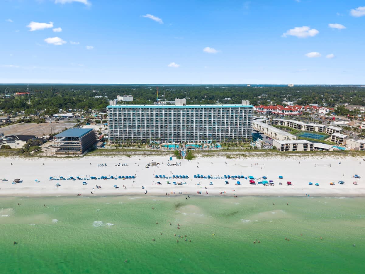 The Summit Penthouse 1501 – Aerial view of a beachfront hotel with pools and beach umbrellas on white sand.