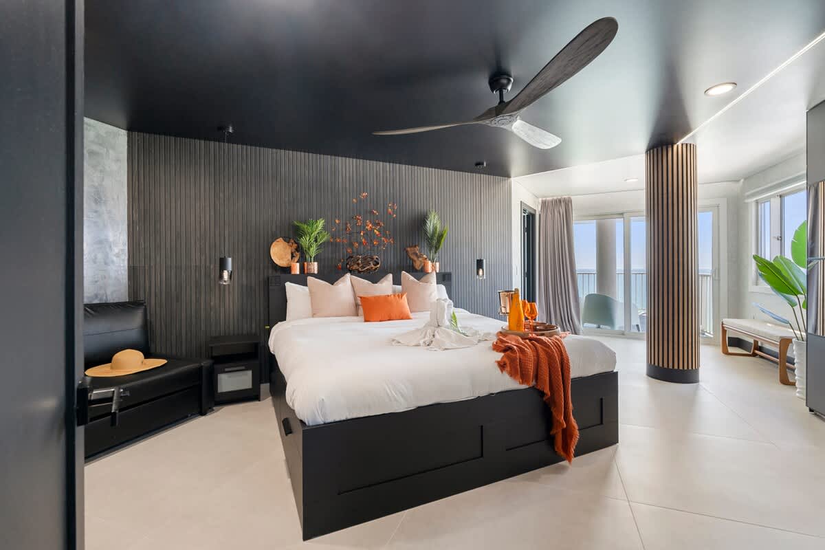 The Summit Penthouse 1501 – Modern bedroom with a large bed, ocean views, seating area, and decorative wall features.