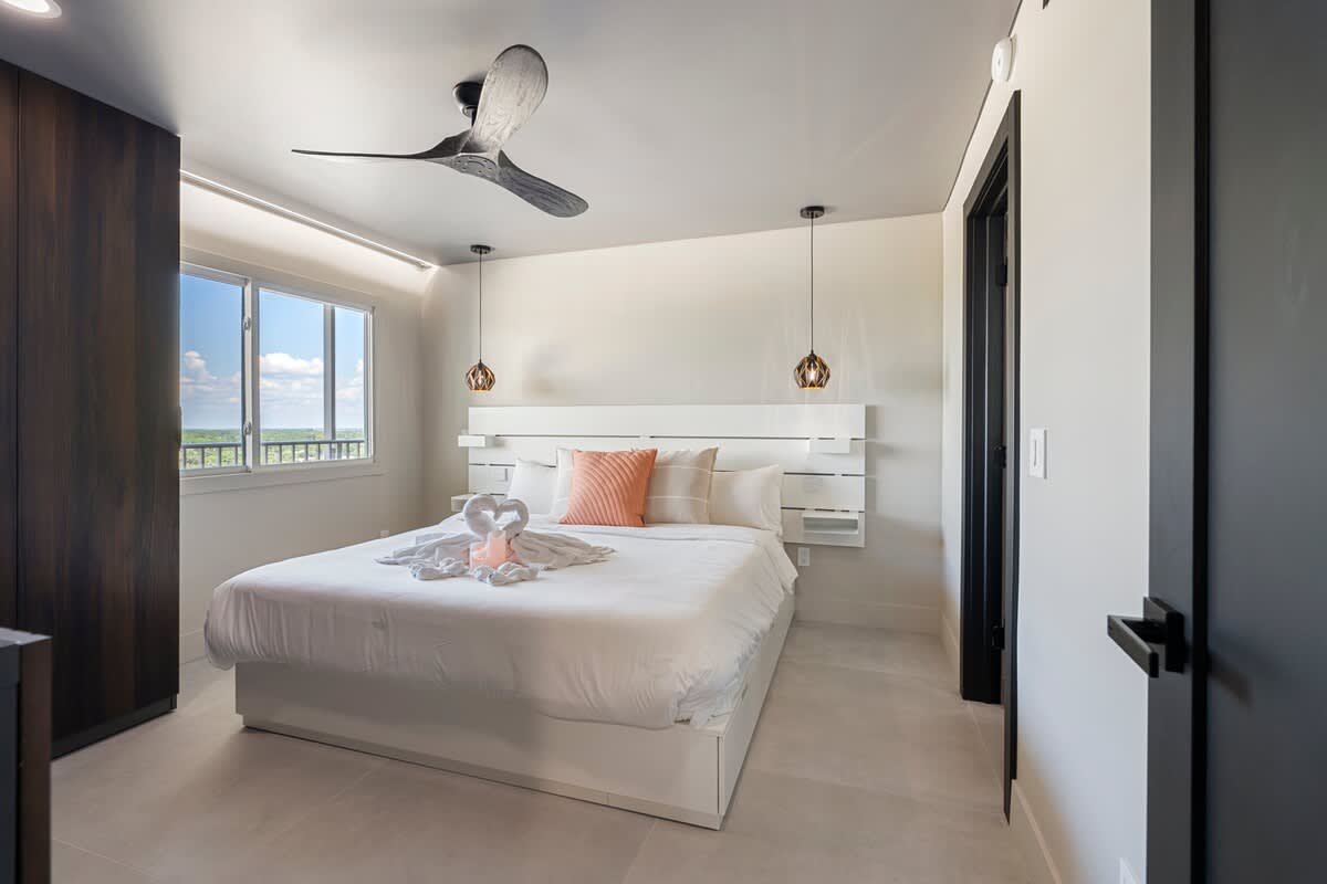 The Summit Penthouse 1501 – Modern bedroom with a large bed, ceiling fan, decorative lighting, and window view.