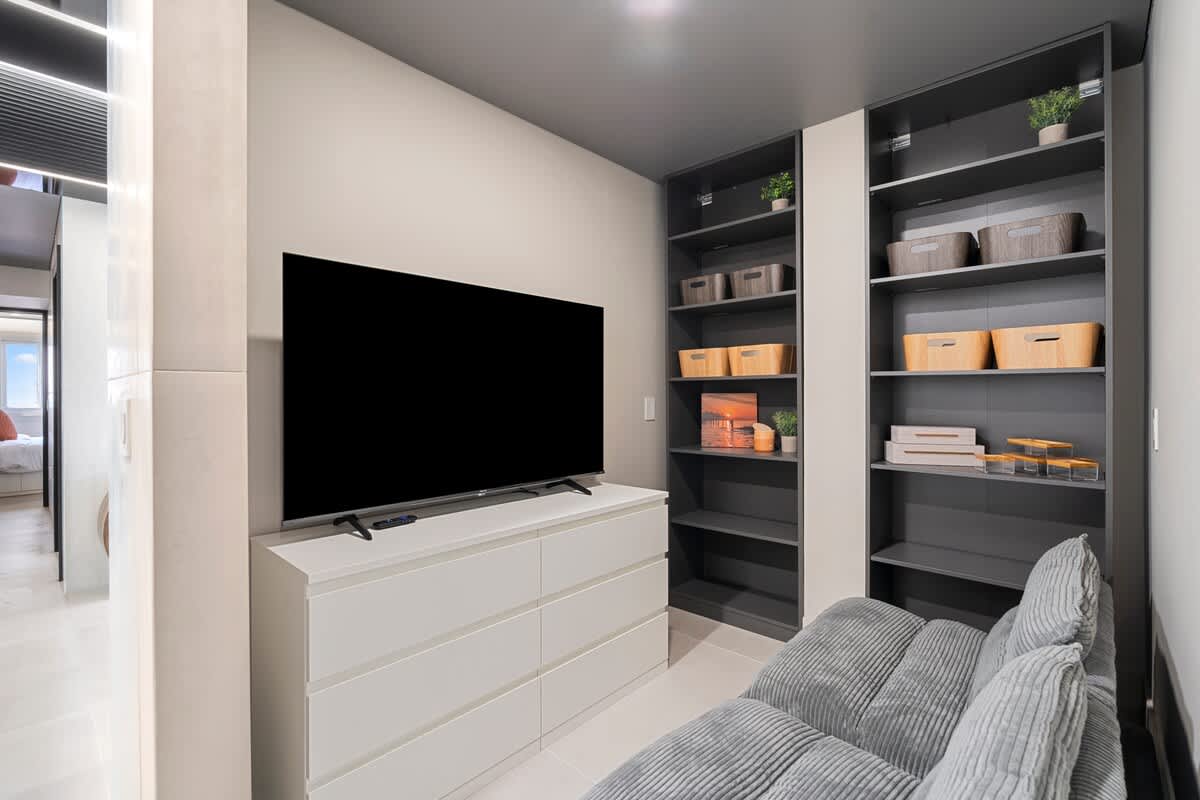 The Summit Penthouse 1501 – Cozy living area with a large TV, gray couch, and shelving for decor and storage.