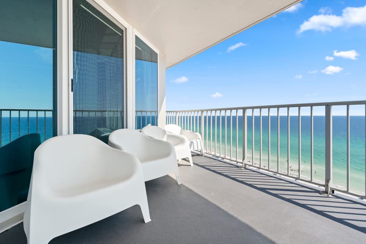 The Summit Penthouse 1501 – Balcony view with white chairs overlooking the ocean and sandy beach.