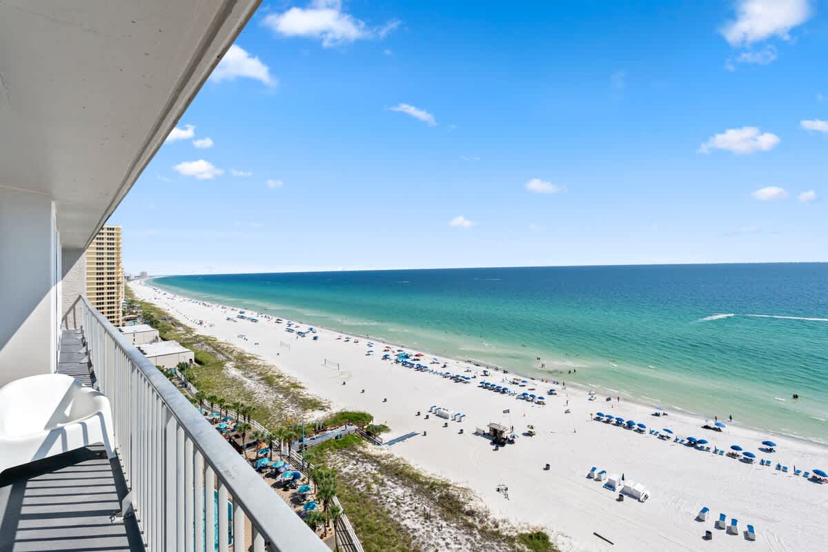 The Summit Penthouse 1501 – Penthouse balcony view overlooking sandy beach, umbrellas, and ocean with clear blue sky.
