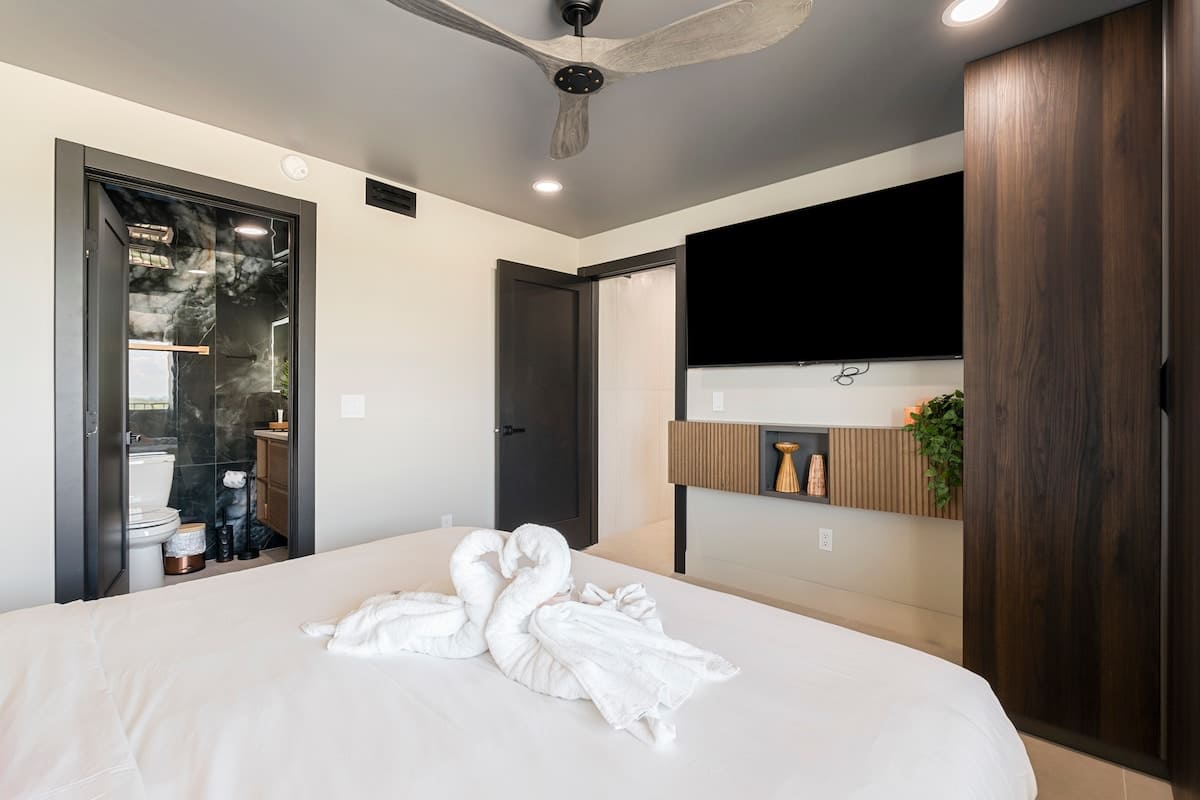 The Summit Penthouse 1501 – Bedroom with a ceiling fan, TV, and bathroom door, featuring a towel arrangement on the bed.