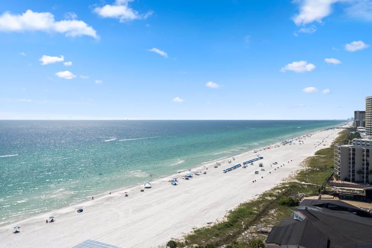 The Summit Penthouse 1501 – View from penthouse showing sandy beach, ocean, and nearby buildings under a clear blue sky.