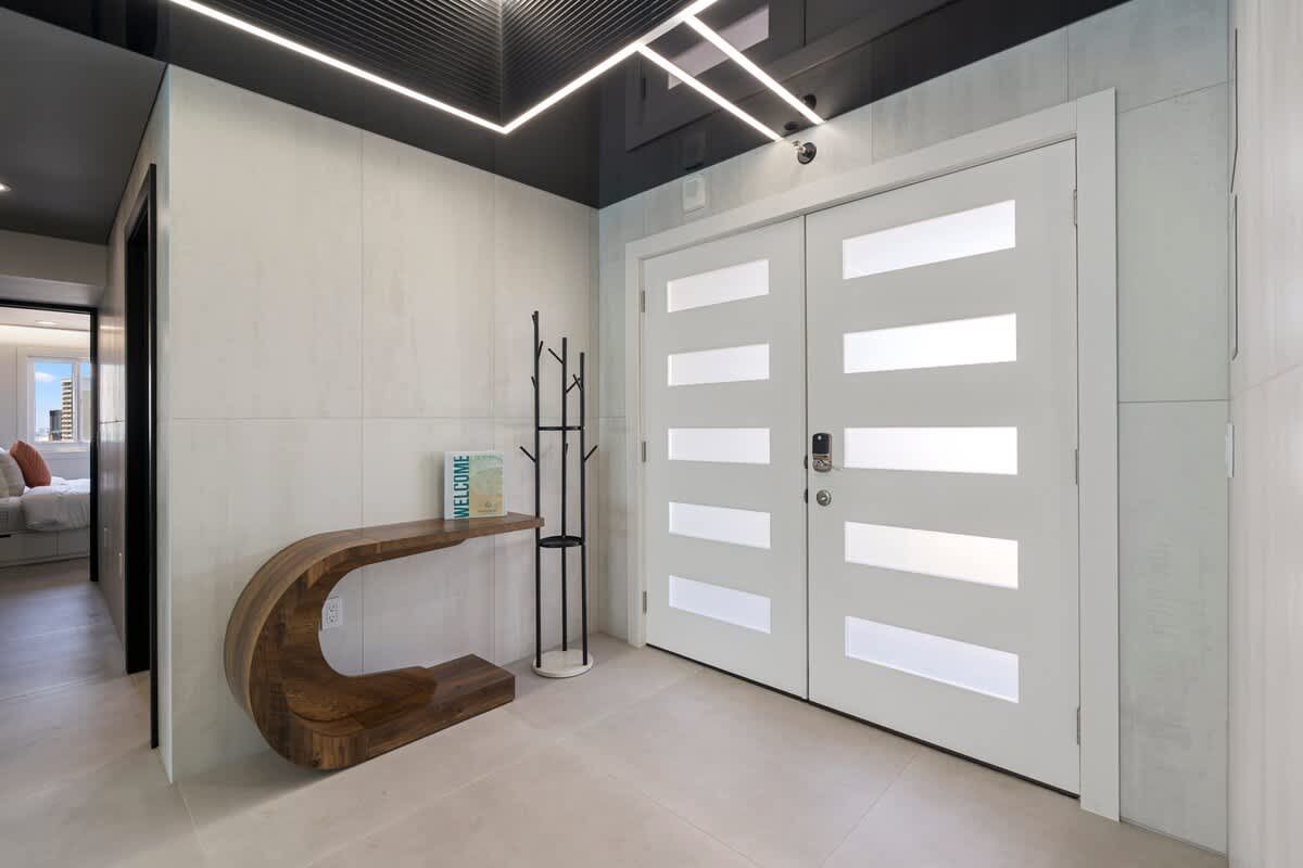 The Summit Penthouse 1501 – Modern entryway with large white doors, wood console table, and coat rack against light-colored walls.