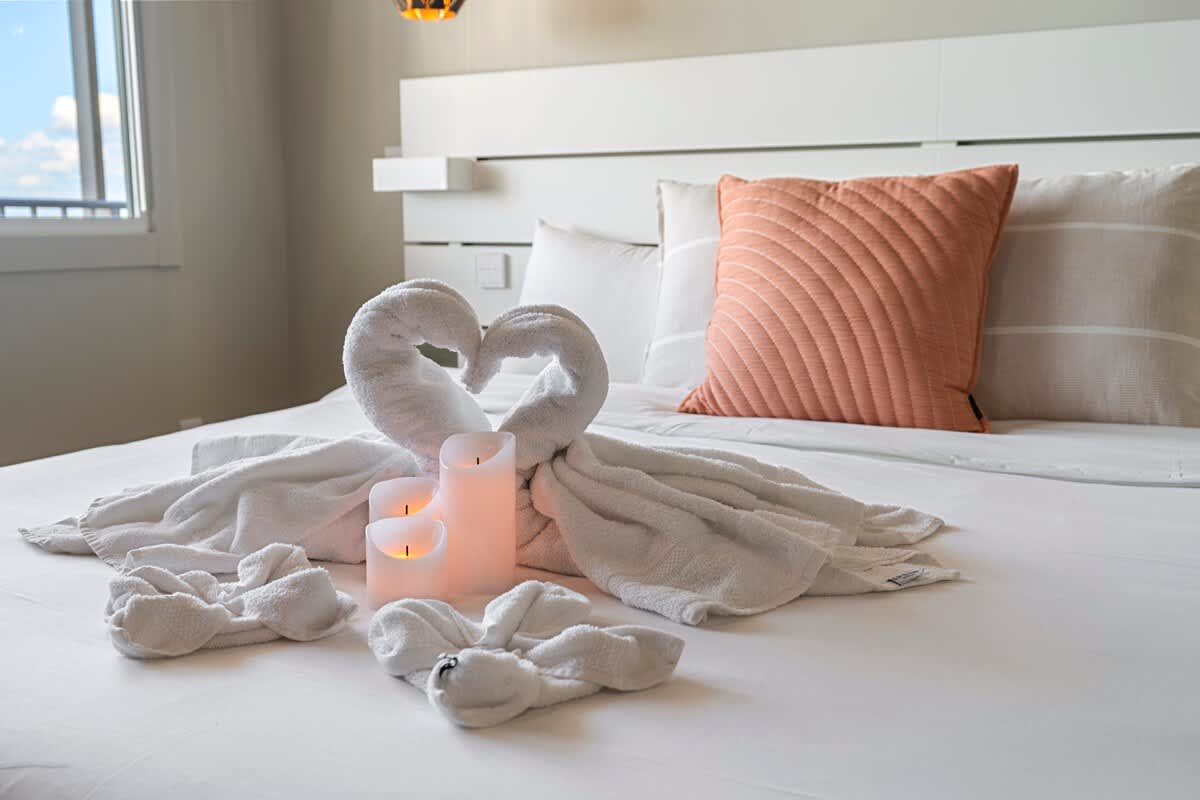 The Summit Penthouse 1501 – King bed with towel swans and candles, accented by a decorative pillow.