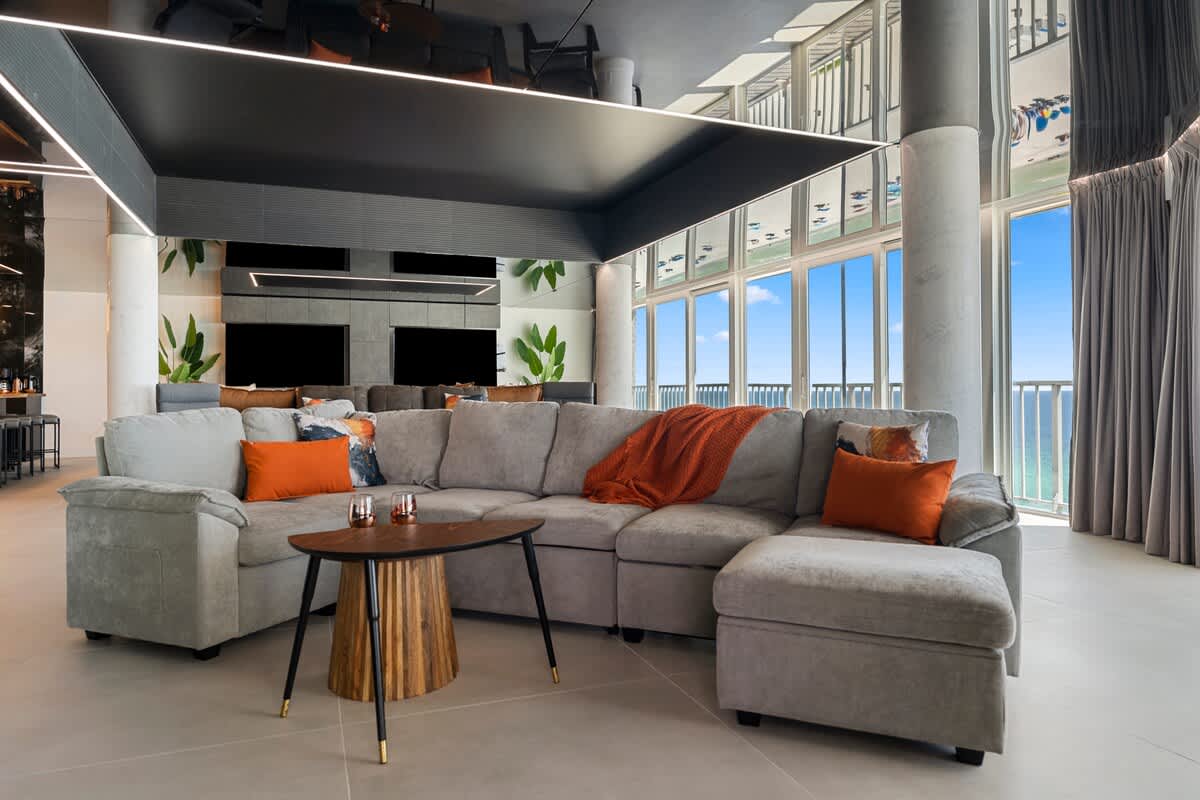 The Summit Penthouse 1501 – Spacious living room with gray sectional, wooden coffee table, large windows, and ocean view.