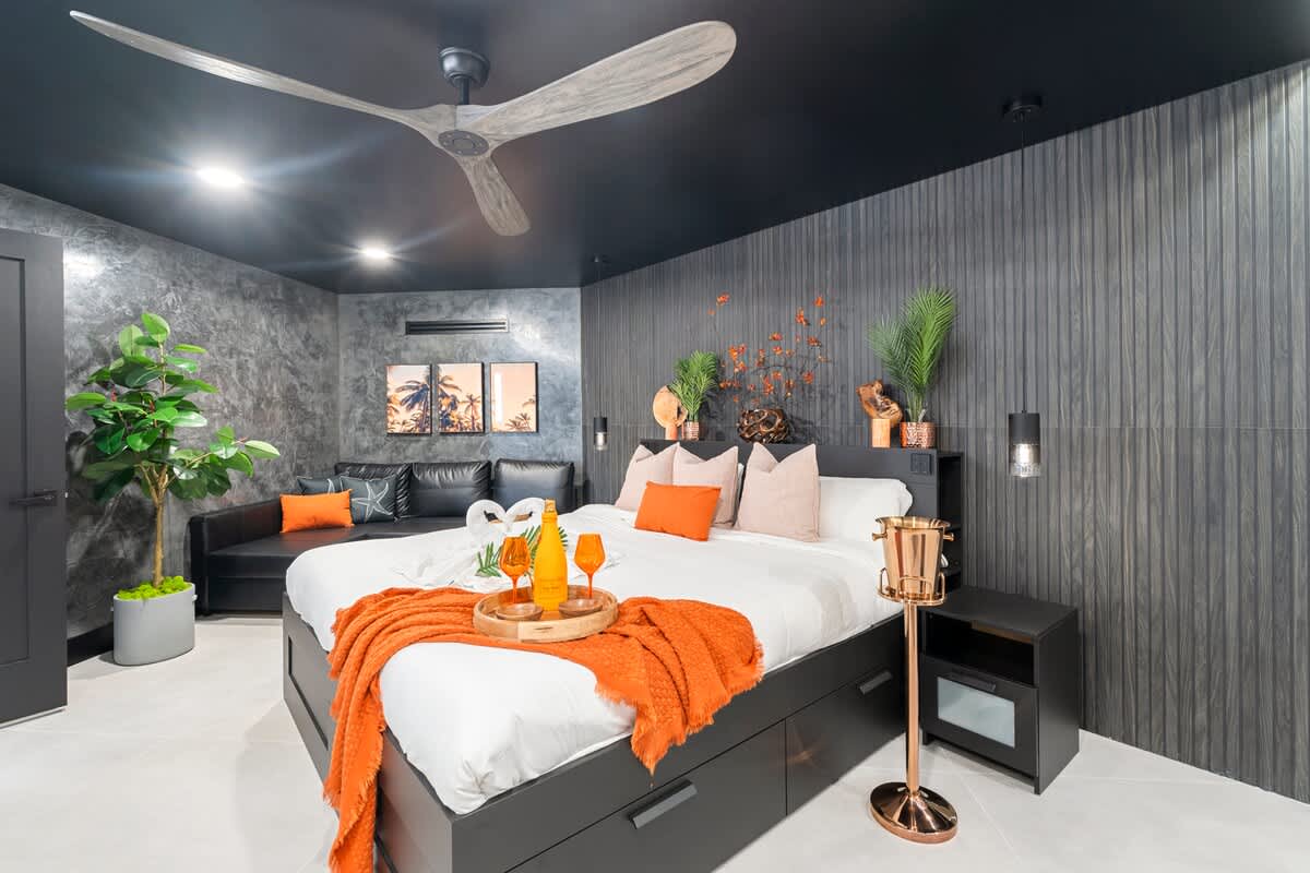 The Summit Penthouse 1501 – Modern bedroom with a king-size bed, black couch, potted plant, and city-view windows.