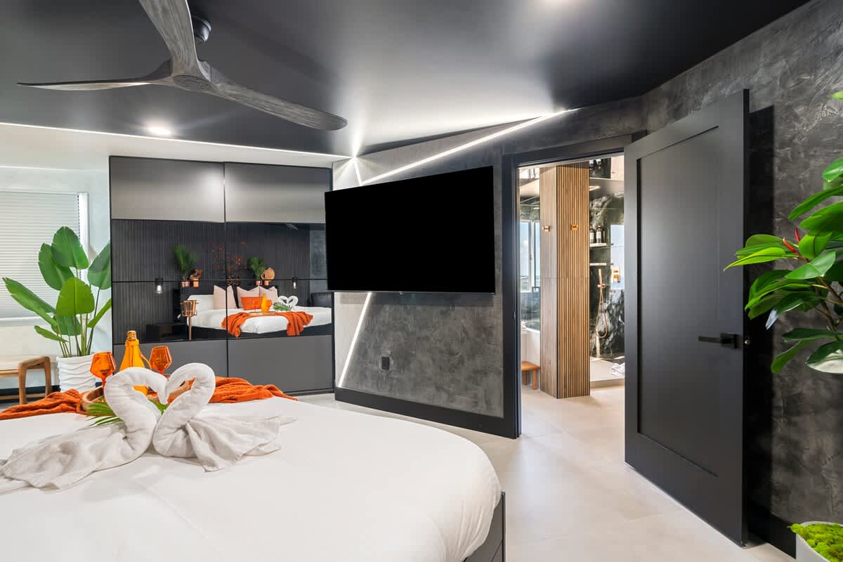 The Summit Penthouse 1501 – Modern bedroom with a large bed, dark accents, ceiling fan, and an en-suite bathroom visible through an open door.