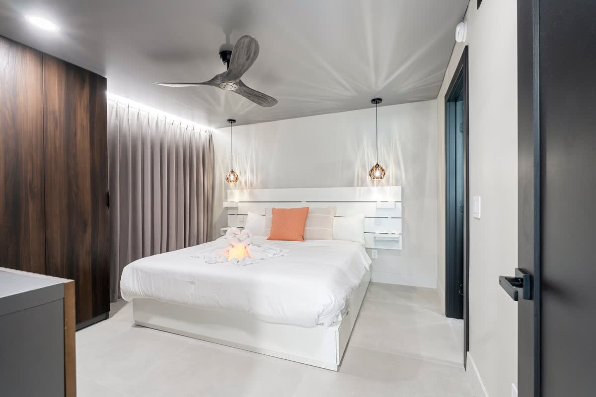 The Summit Penthouse 1501 – Modern bedroom with a king-sized bed, ceiling fan, and pendant lighting, featuring gray curtains and dark wood accents.