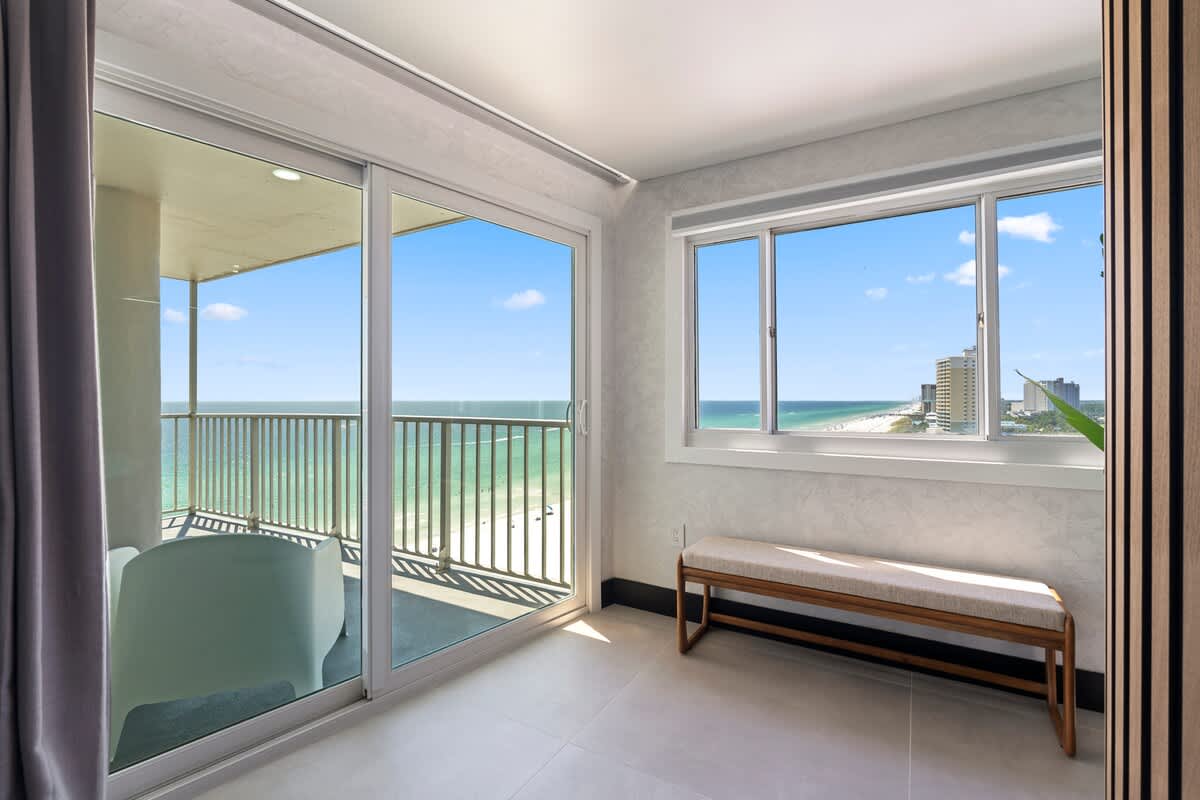 The Summit Penthouse 1501 – Penthouse sitting area with large windows showcasing ocean view and balcony, featuring a bench and modern decor.