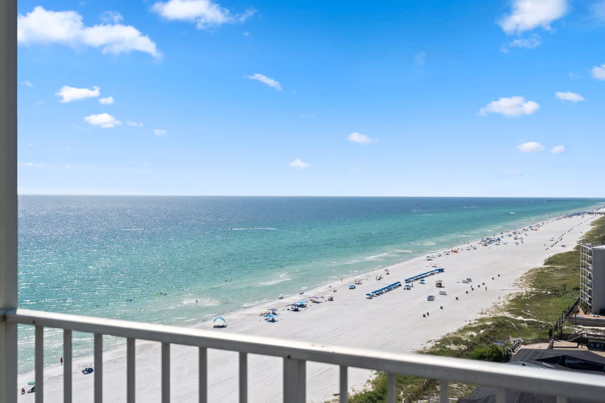 The Summit Penthouse 1501 – Ocean view from a penthouse balcony overlooking a sandy beach with umbrellas and people.