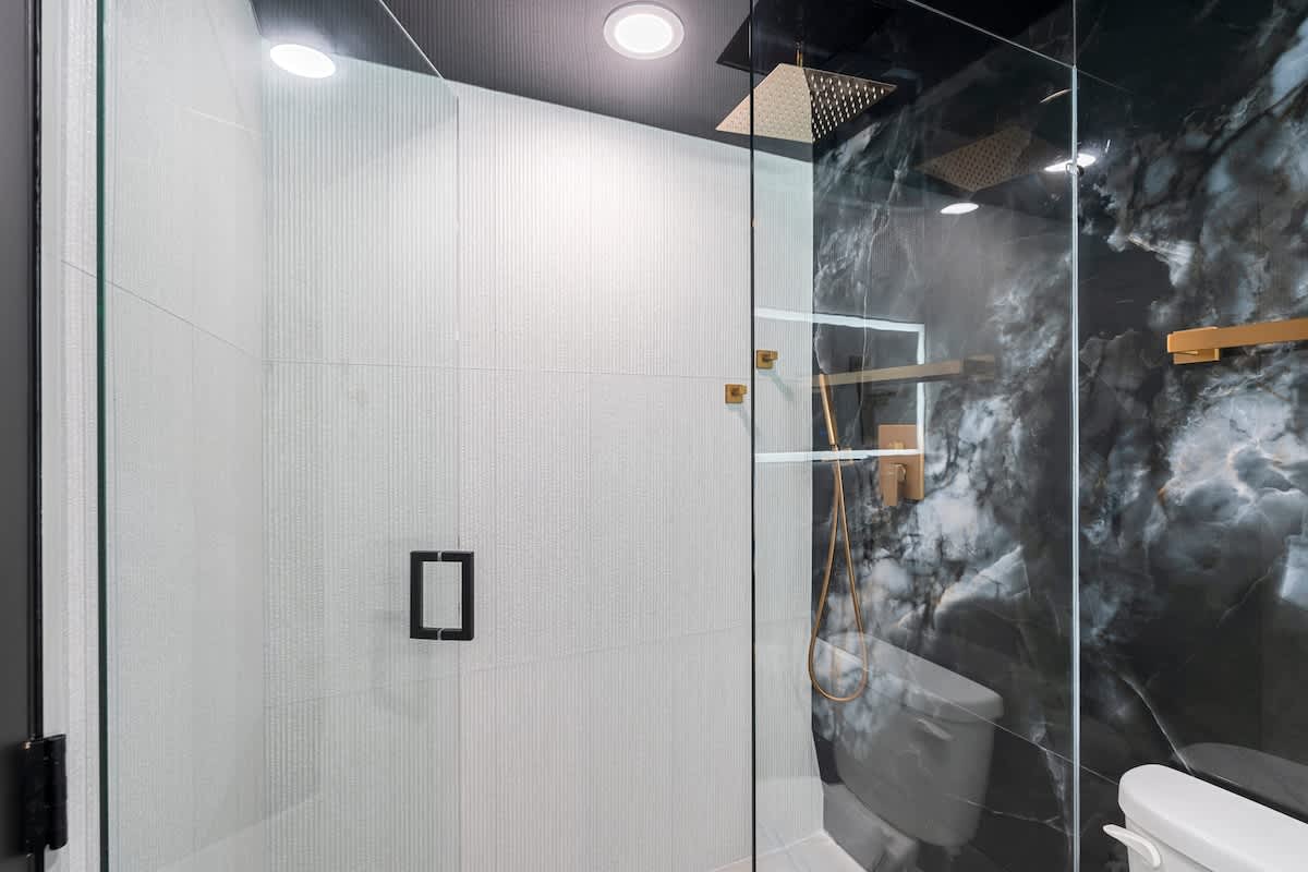 The Summit Penthouse 1501 – Modern glass shower with textured walls, marble accent, and gold fixtures.