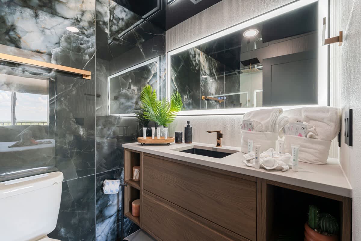 The Summit Penthouse 1501 – Modern bathroom with dark marble walls, wooden vanity, sink, and neatly arranged toiletries.