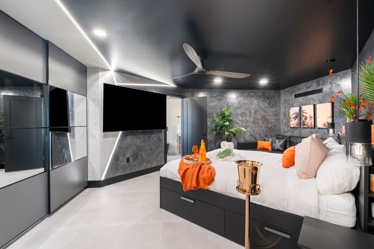 The Summit Penthouse 1501 – Modern bedroom with a king bed, large TV, and a view of palm trees through windows.