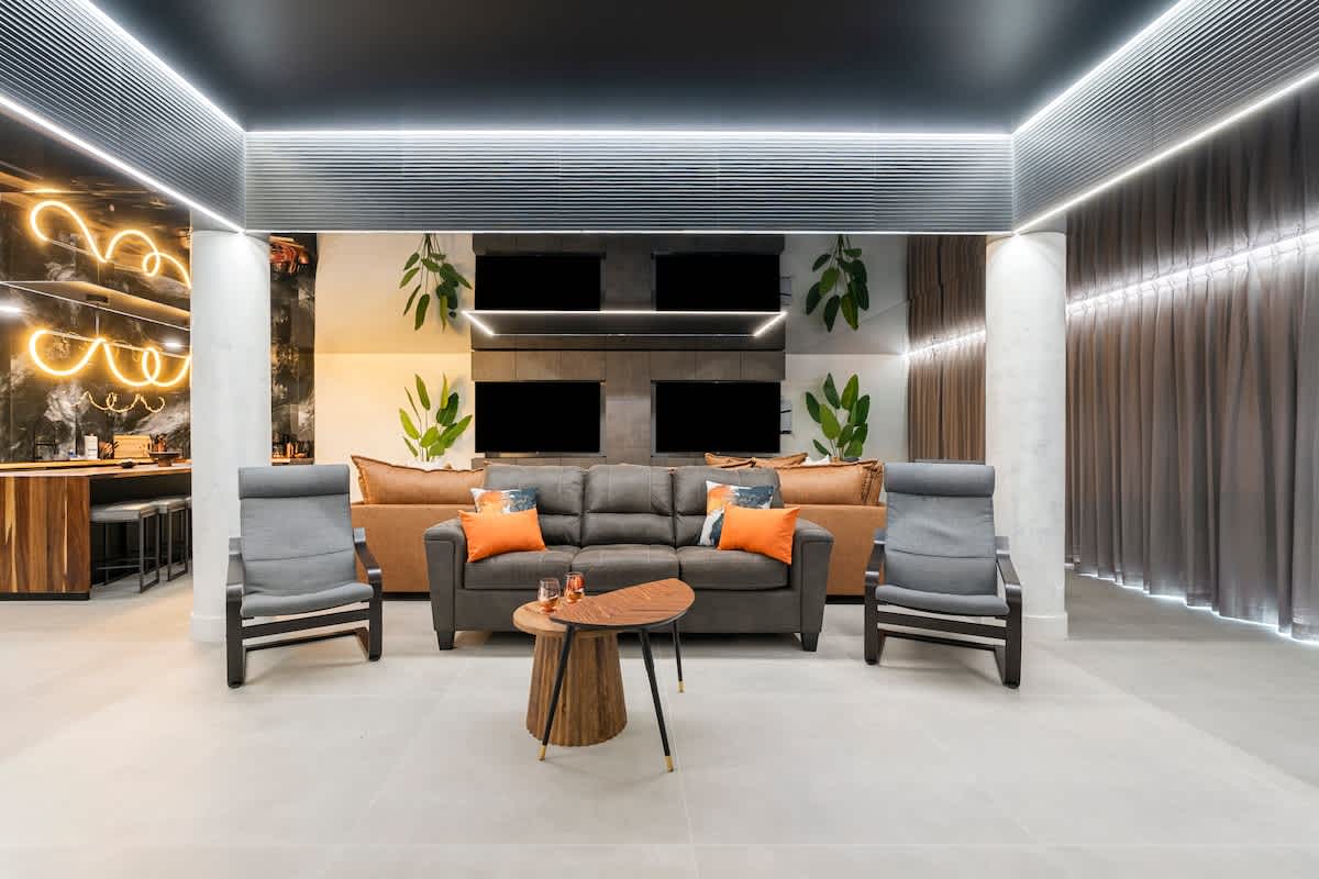 The Summit Penthouse 1501 – Modern living room with gray couch, orange accents, two chairs, and wall-mounted televisions.