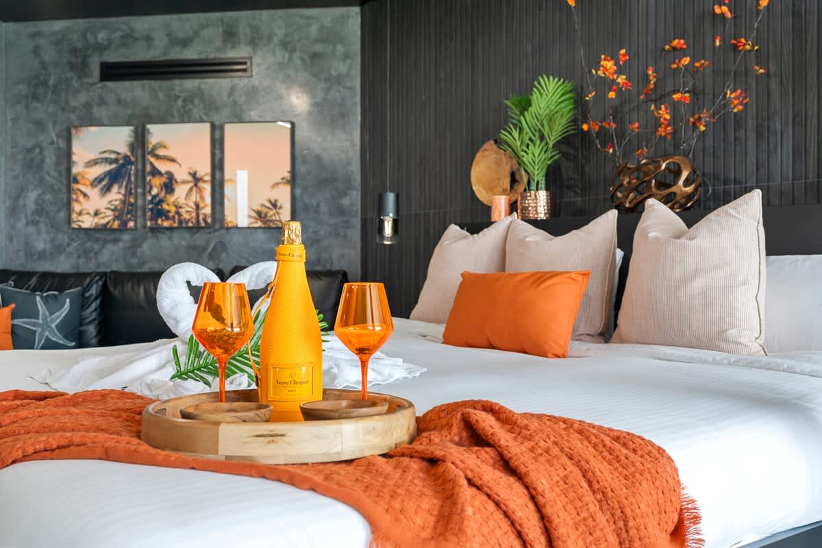 The Summit Penthouse 1501 – Stylish bedroom with king bed, decorative pillows, orange accents, champagne, and tropical artwork.