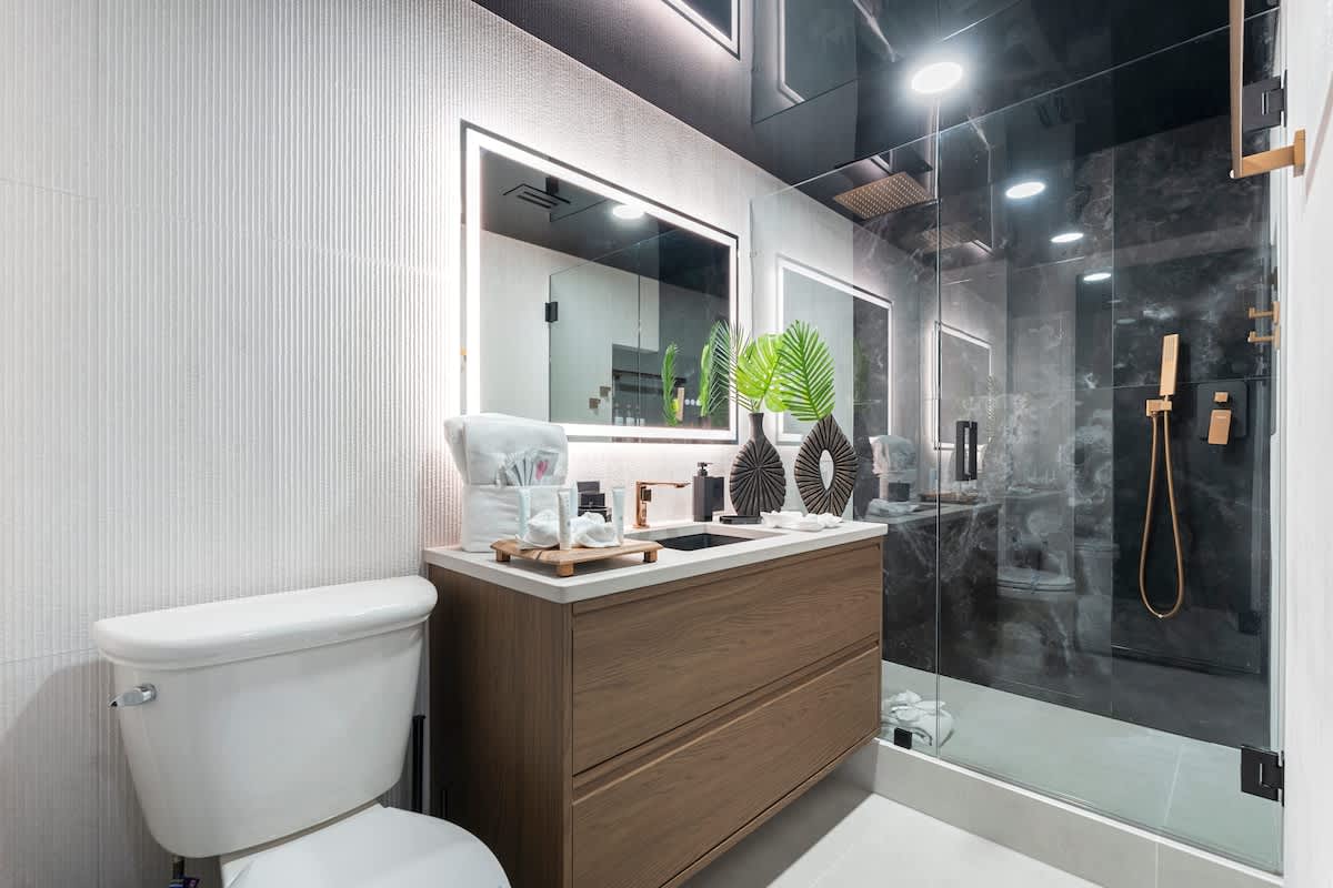 The Summit Penthouse 1501 – Modern bathroom with a glass shower, wooden vanity, two mirrors, and decorative plants.