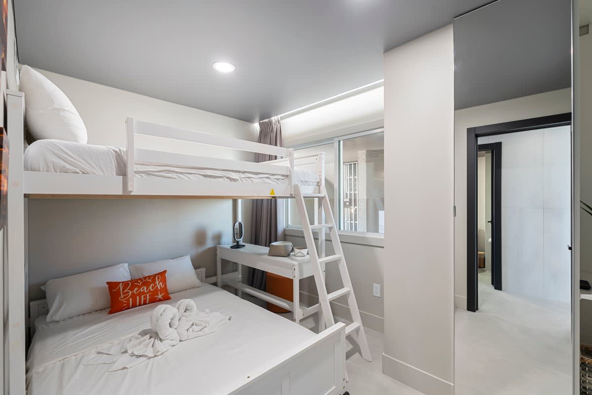 The Summit Penthouse 1501 – Bunk bed and queen bed in a bright, modern bedroom with a window and small desk.