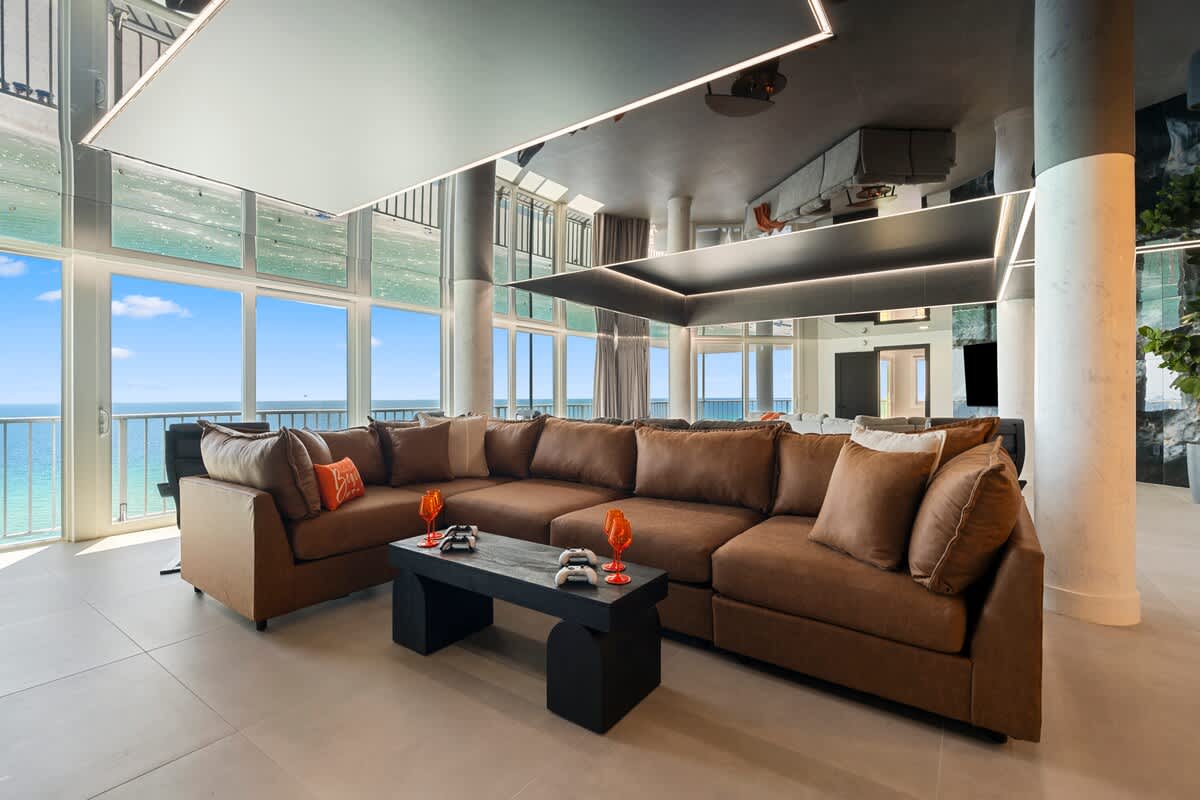 The Summit Penthouse 1501 – Living room with brown sectional sofa, ocean view, and large windows.