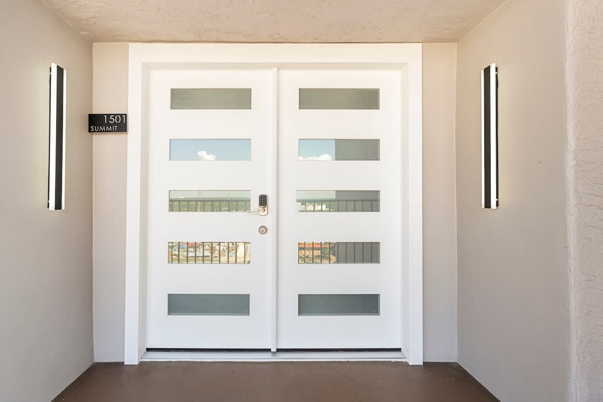 The Summit Penthouse 1501 – Modern entrance with white double doors, nameplate, and wall sconces, leading to Summit Penthouse 1501.