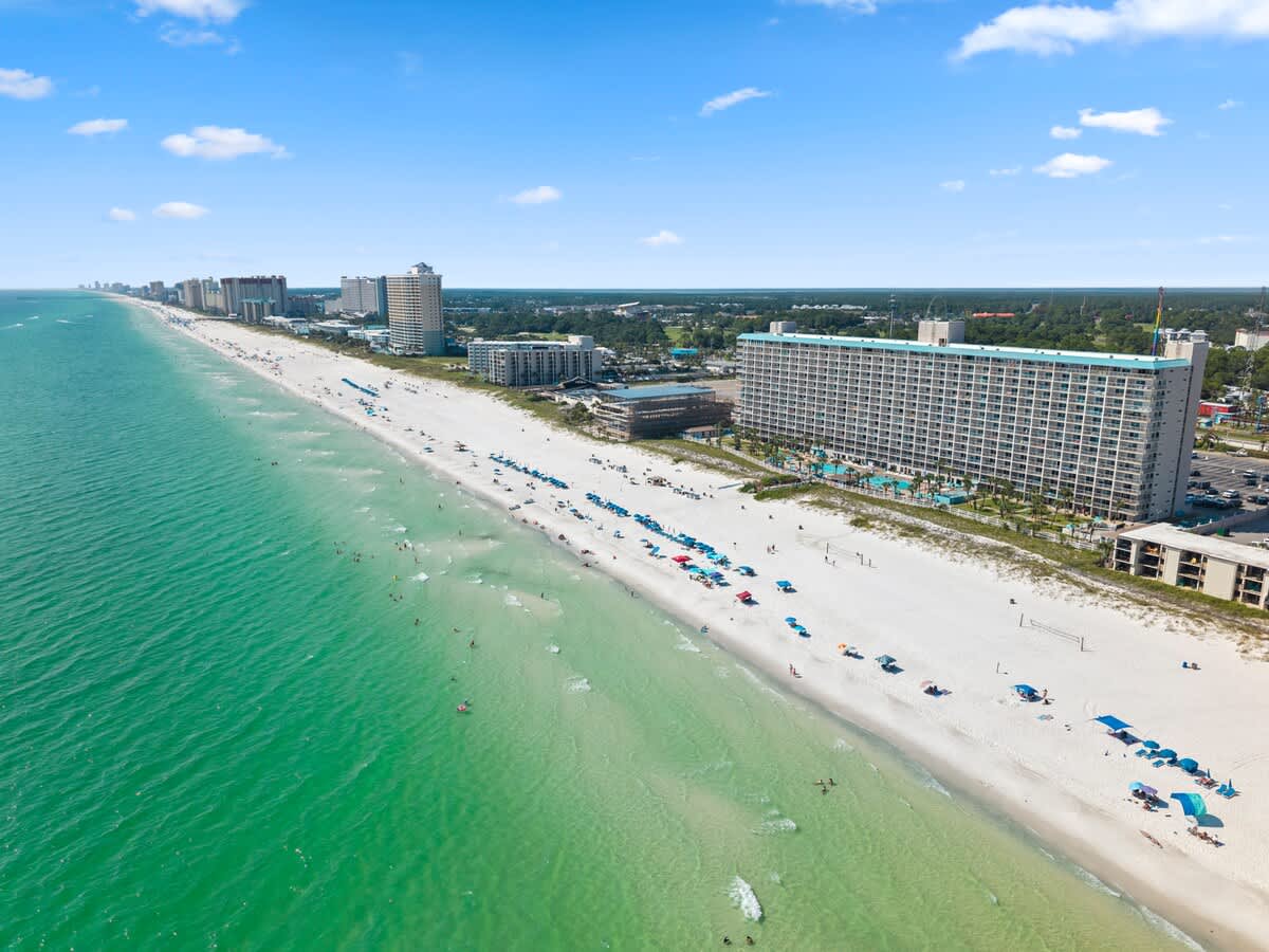 The Summit Penthouse 1501 – Aerial view of a sandy beach with umbrellas, hotels, and turquoise water.
