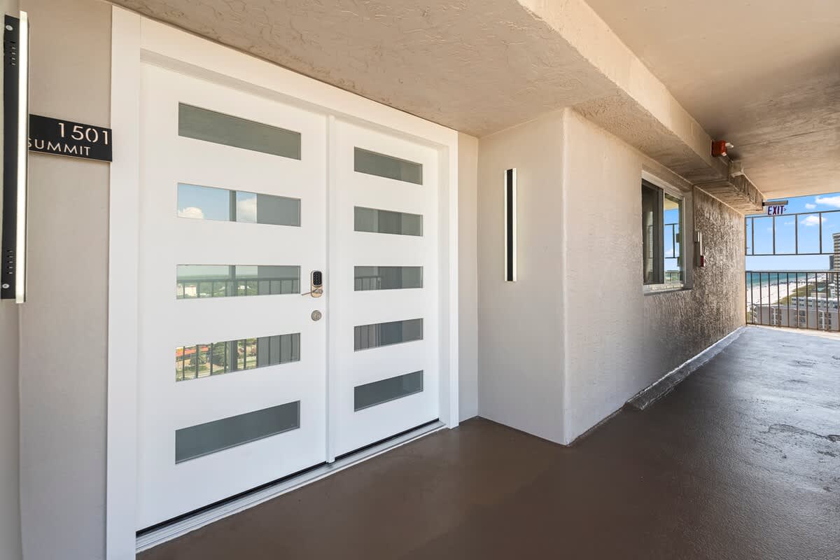 The Summit Penthouse 1501 – Entryway of a penthouse with double doors, wall-mounted lights, and an ocean view in the background.