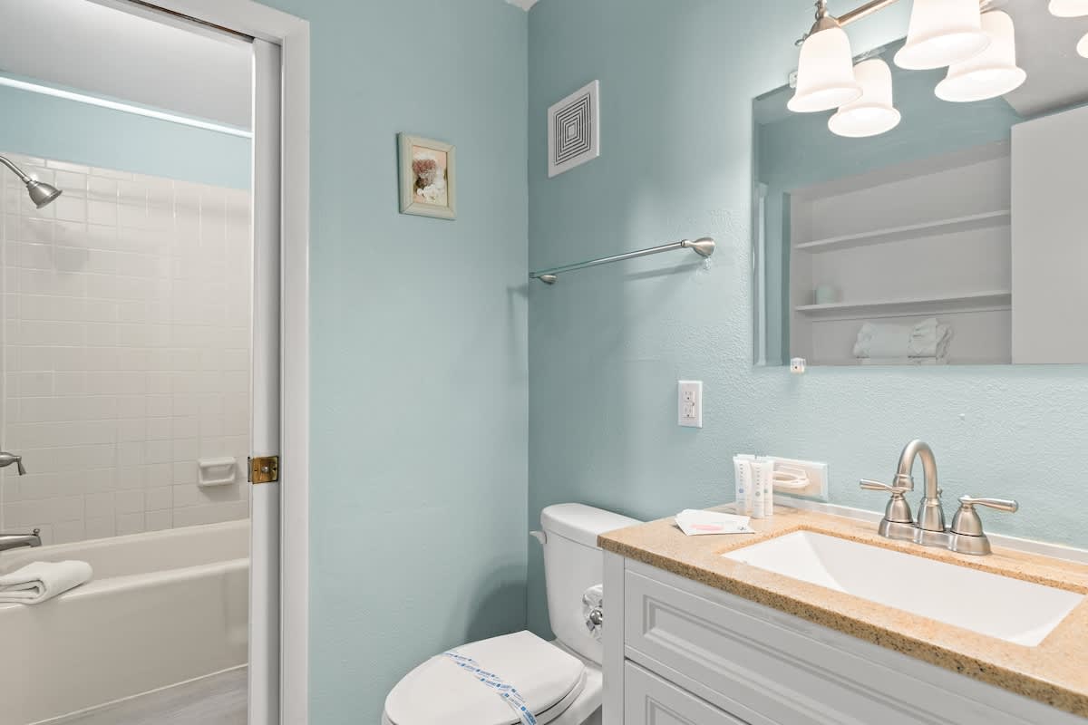 The Summit 315 – Bathroom with light blue walls, white tub, sink with beige countertop, and toiletries on the counter.