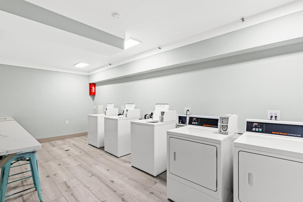 The Summit 315 – Laundry room with multiple white washers and dryers, light gray walls, and a folding table.