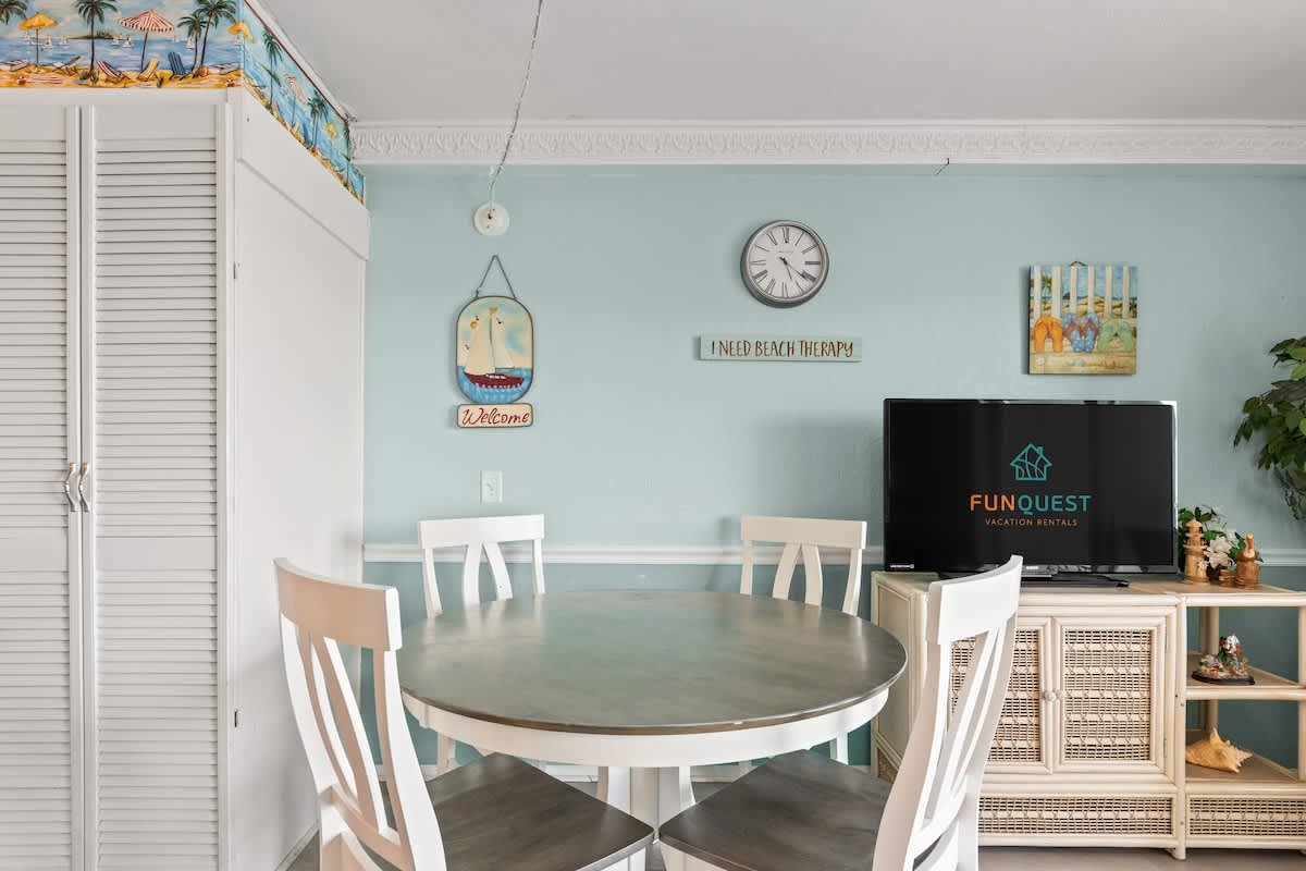 The Summit 315 – Dining area with a round table, white chairs, wall decorations, and a TV on a cabinet.