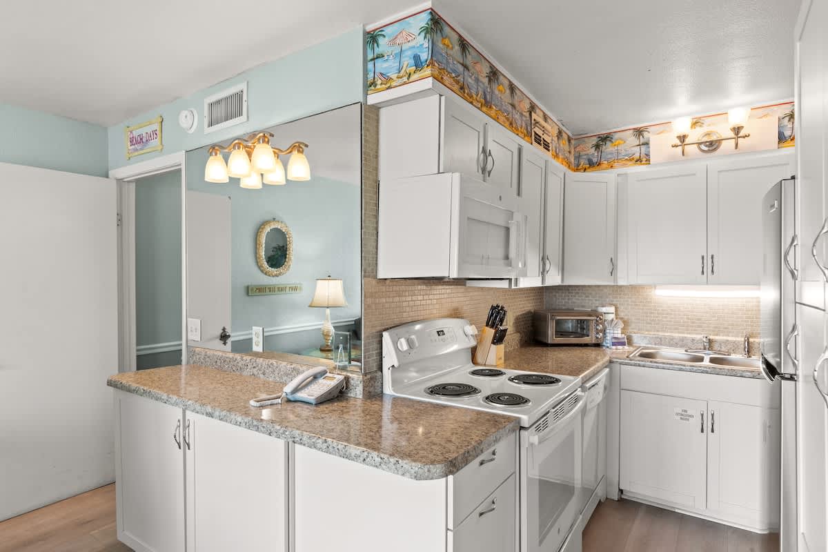 The Summit 315 – Bright kitchen with white cabinets, granite countertops, stove, sink, and decorative wallpaper.