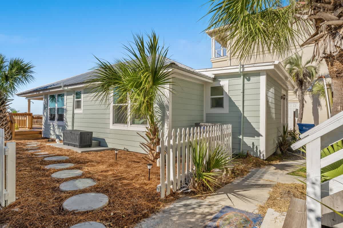 9620 Beach Blvd – Single-story beach house exterior with green siding, palm trees, and a stone pathway.