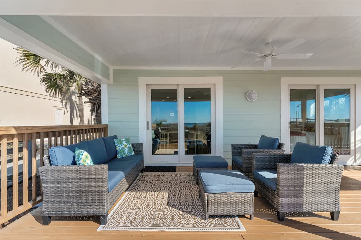 9620 Beach Blvd – Covered patio with seating, decorative rug, and view through sliding glass doors. Palm trees visible outside.