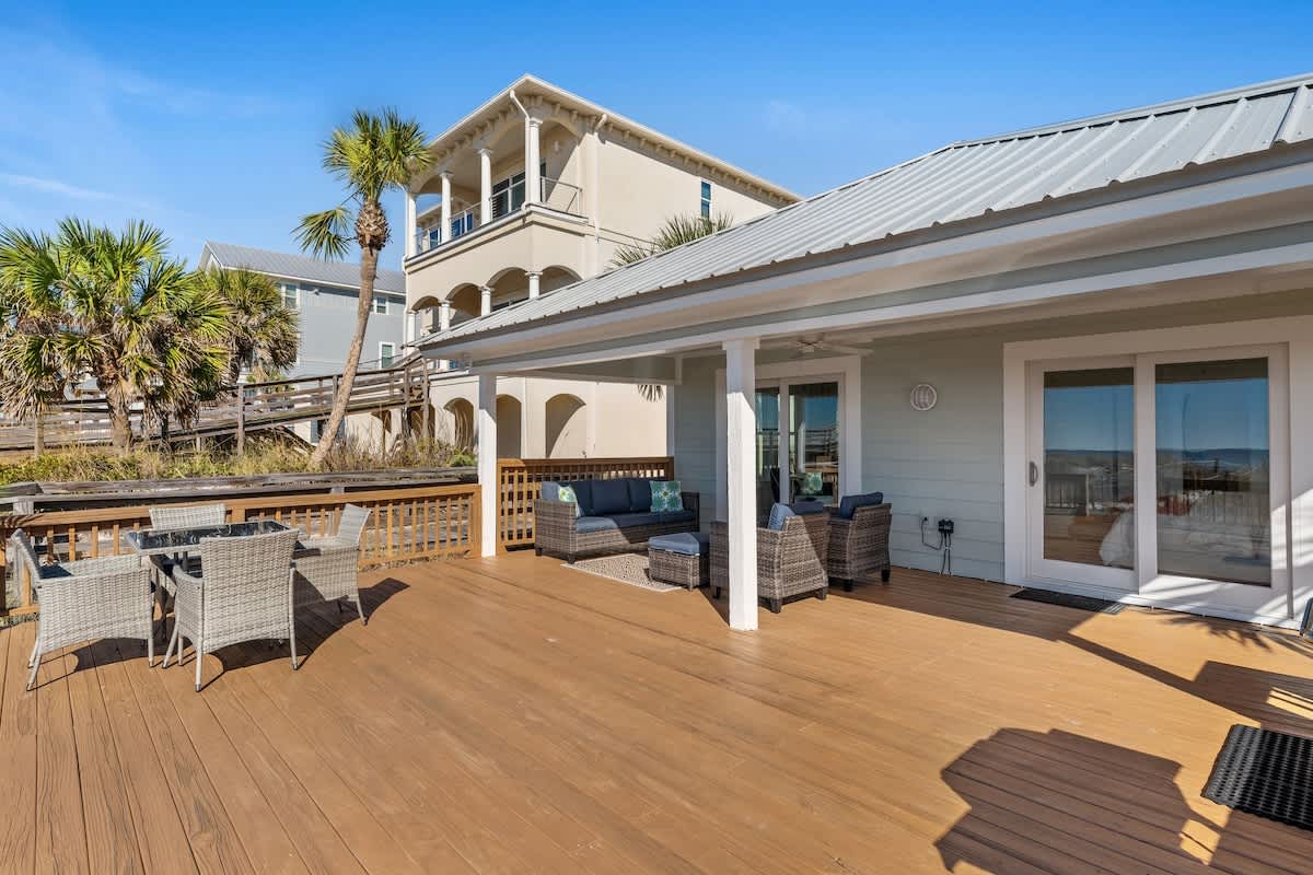 9620 Beach Blvd – Spacious wooden deck with outdoor seating and palm trees, adjacent to a beachside rental property.