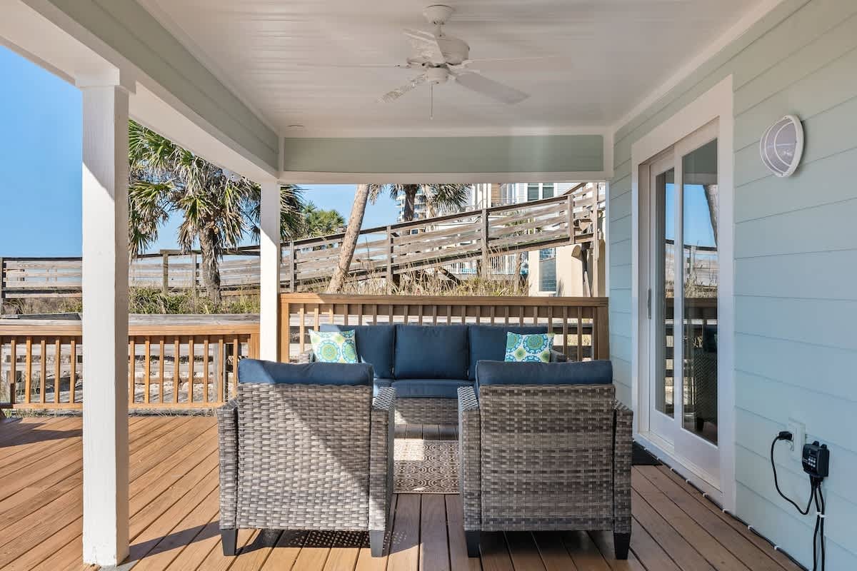 9620 Beach Blvd – Covered patio with wicker furniture, palm trees, and a view of nearby wooden steps leading to the beach.