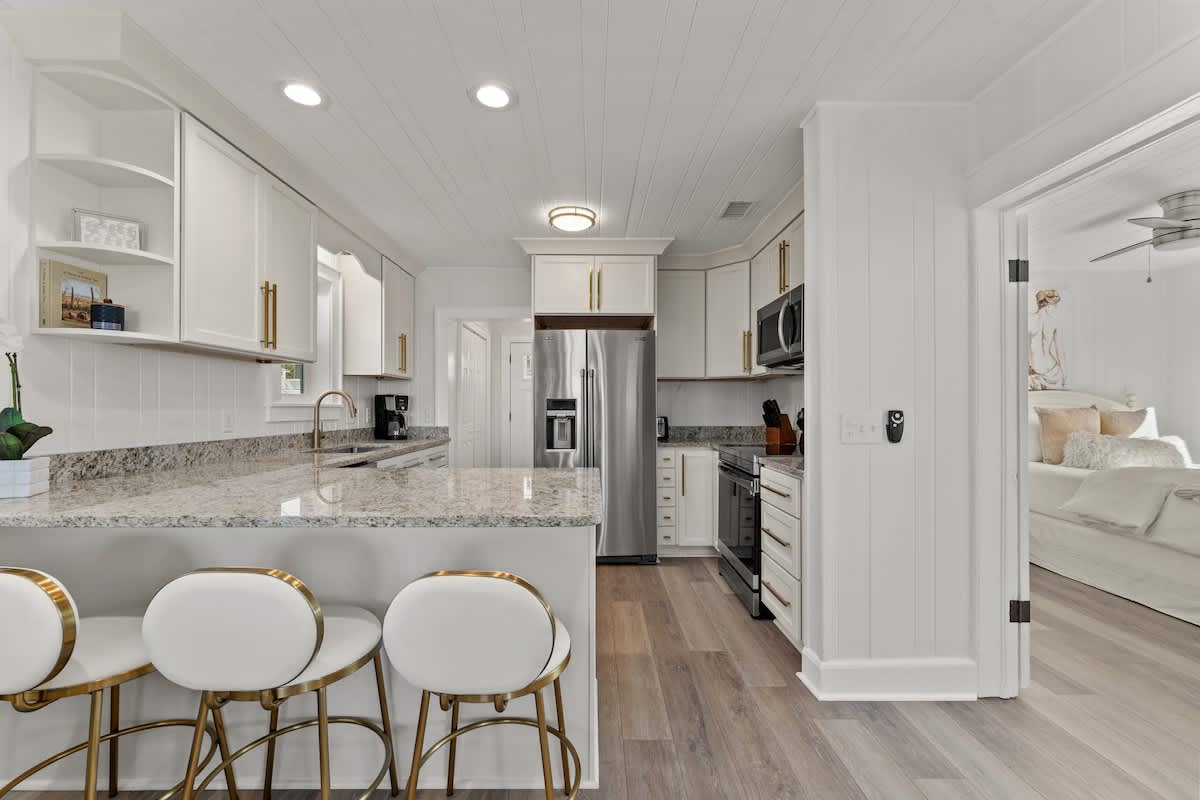 9620 Beach Blvd – Bright kitchen with white cabinetry, granite countertops, and modern appliances; bar seating visible. Bedroom visible through doorway.