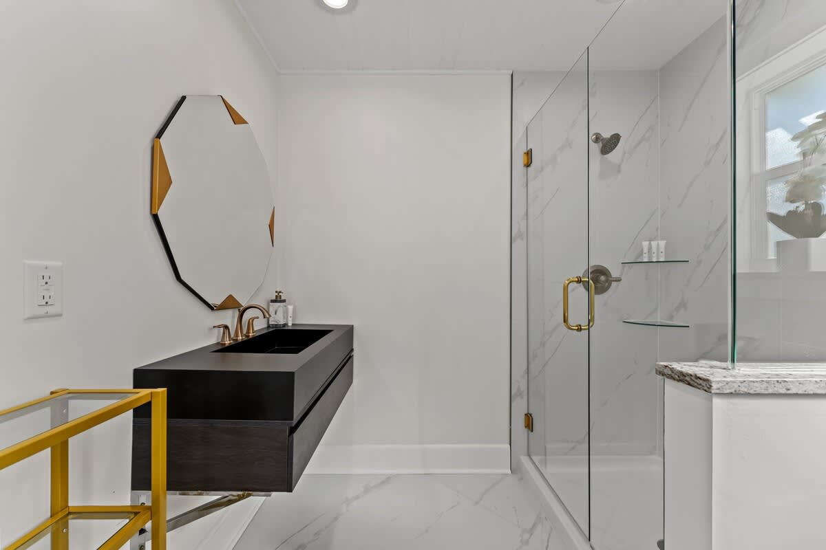 9620 Beach Blvd – Modern bathroom featuring a glass shower, black vanity, gold accents, and a large mirror.