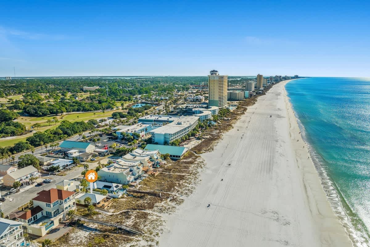9620 Beach Blvd – Aerial view of beachfront property with white sand, nearby buildings, and a clear blue sky.