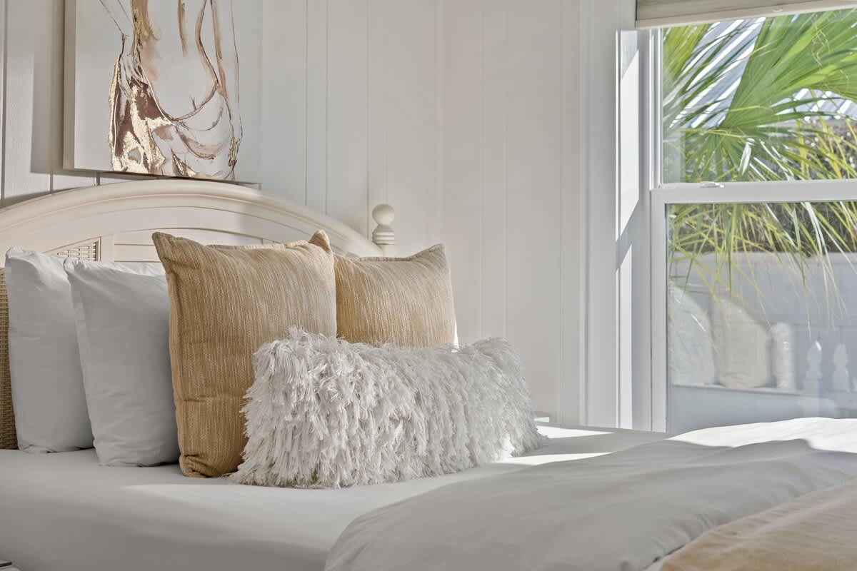9620 Beach Blvd – Cozy bedroom with a large bed, decorative pillows, and a view of palm trees outside the window.