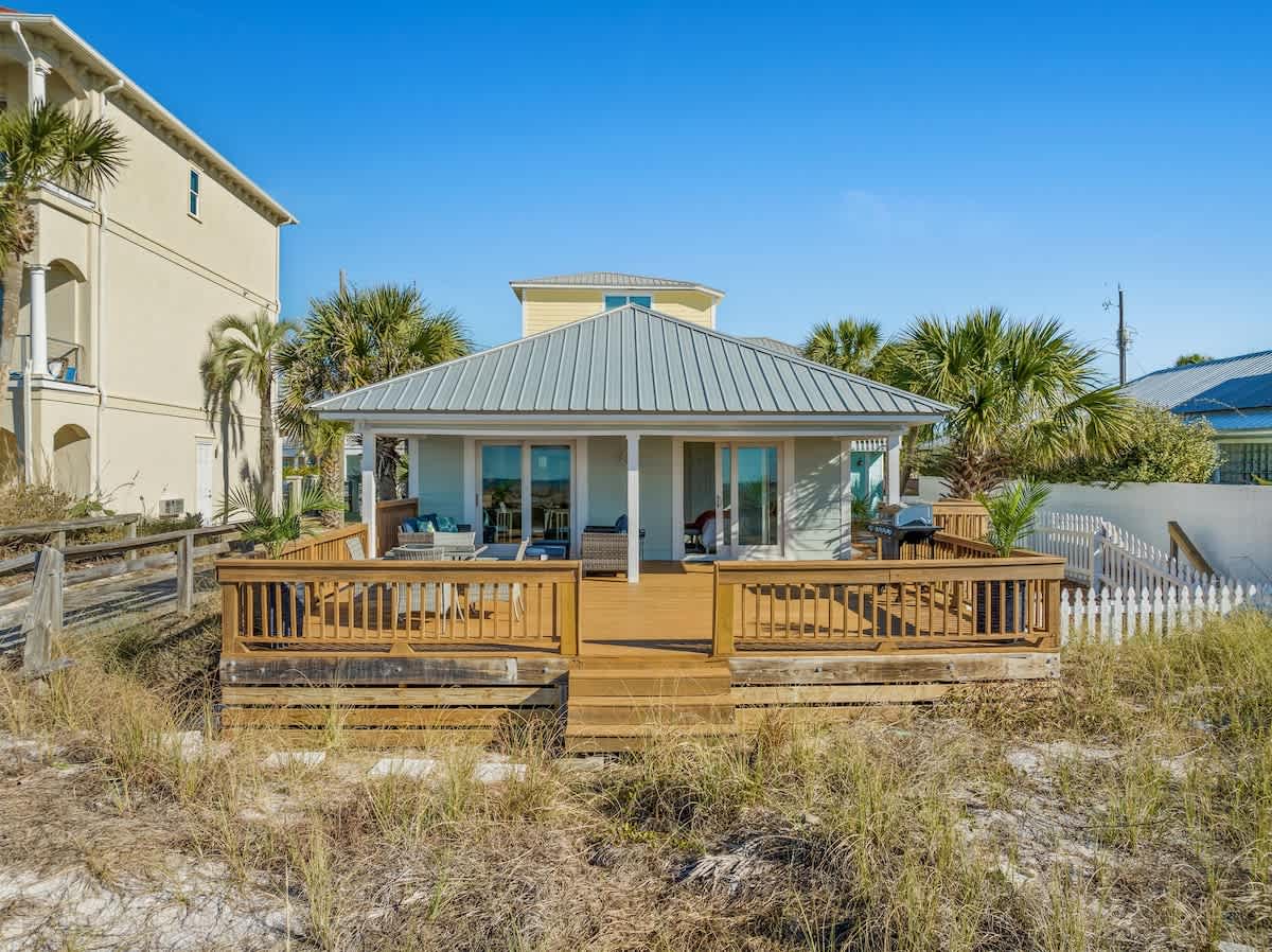 9620 Beach Blvd – Single-story beach house with a wraparound deck and sliding glass doors, surrounded by tall grass and palm trees.