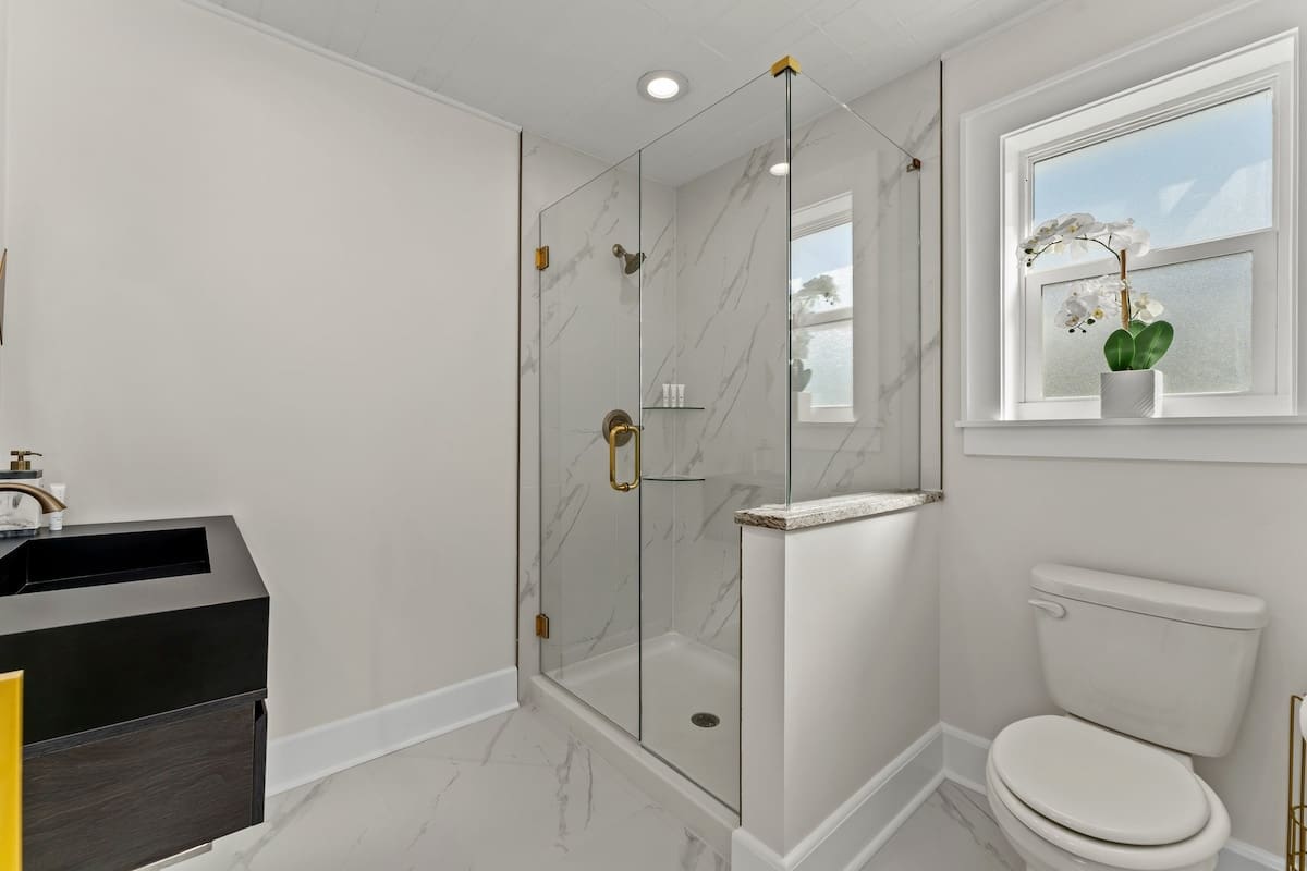 9620 Beach Blvd – Modern bathroom featuring a glass shower, dark sink cabinet, and window with decorative plant.