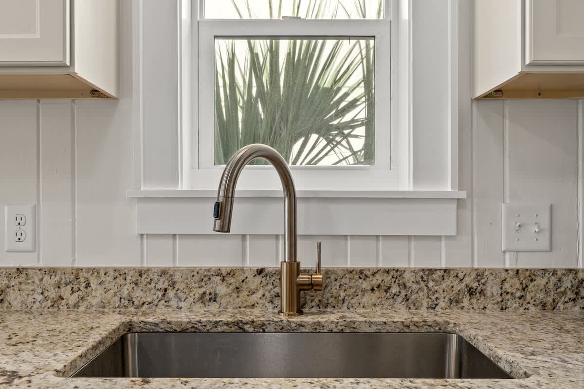 9620 Beach Blvd – Kitchen sink with a modern faucet, granite countertop, and a window showing greenery outside.