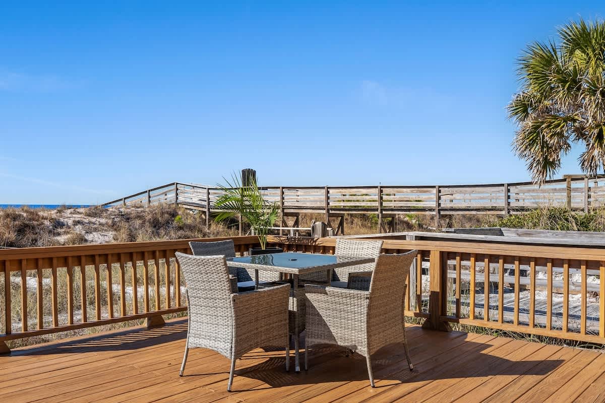 9620 Beach Blvd – Outdoor deck with a table and chairs, palm trees, and a view of a nearby boardwalk and ocean.